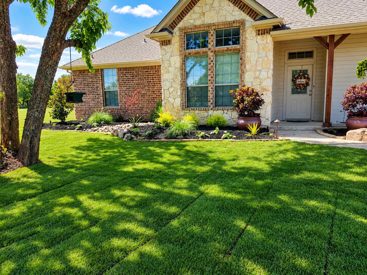 Stone and brick home with a fresh, even lawn and planted beds
