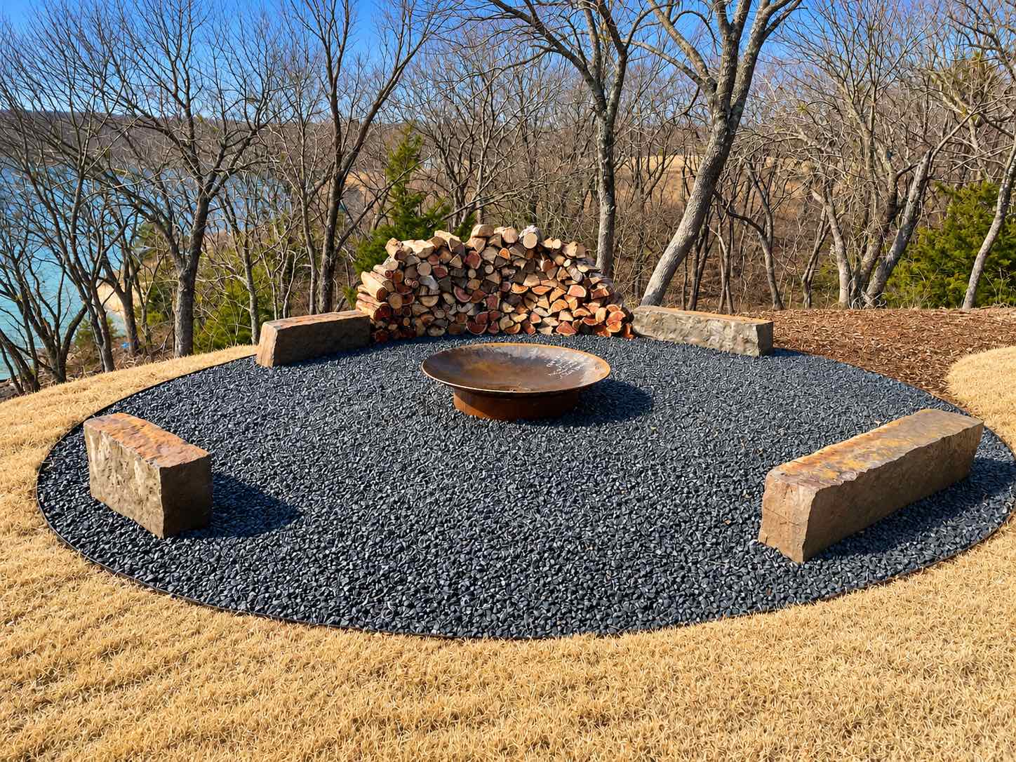 Fire pit on a black gravel circle with stone block seating above a lake
